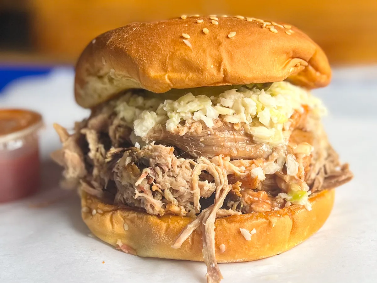 Close-up of a pulled pork BBQ sandwich piled with fresh-chopped pit-smoked pork and slaw on a sesame seed bun