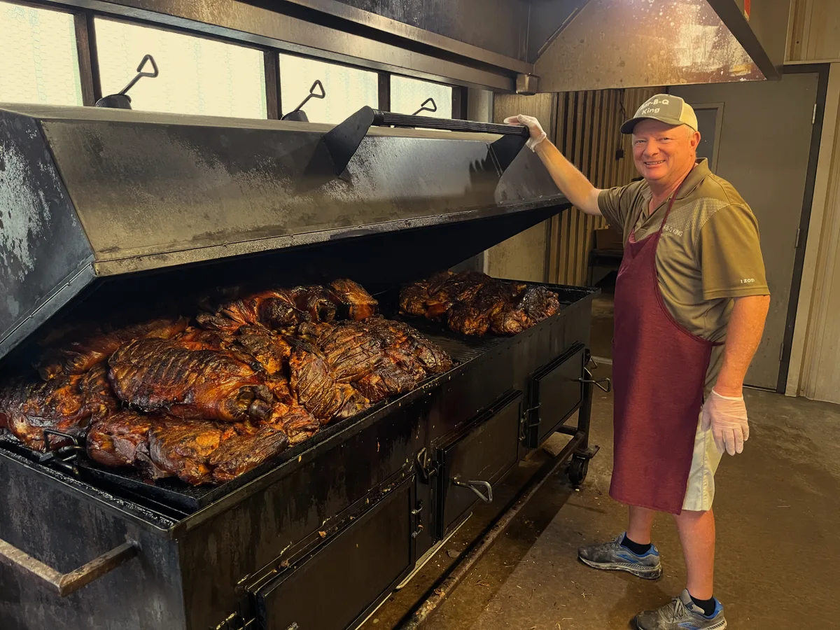 BBQ King staff member at the open pit smoker loaded with pork shoulders